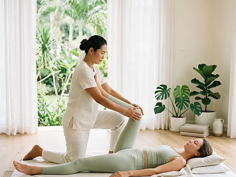 Futon Thai massage — an assisted leg stretch on a floor mat, the client fully clothed